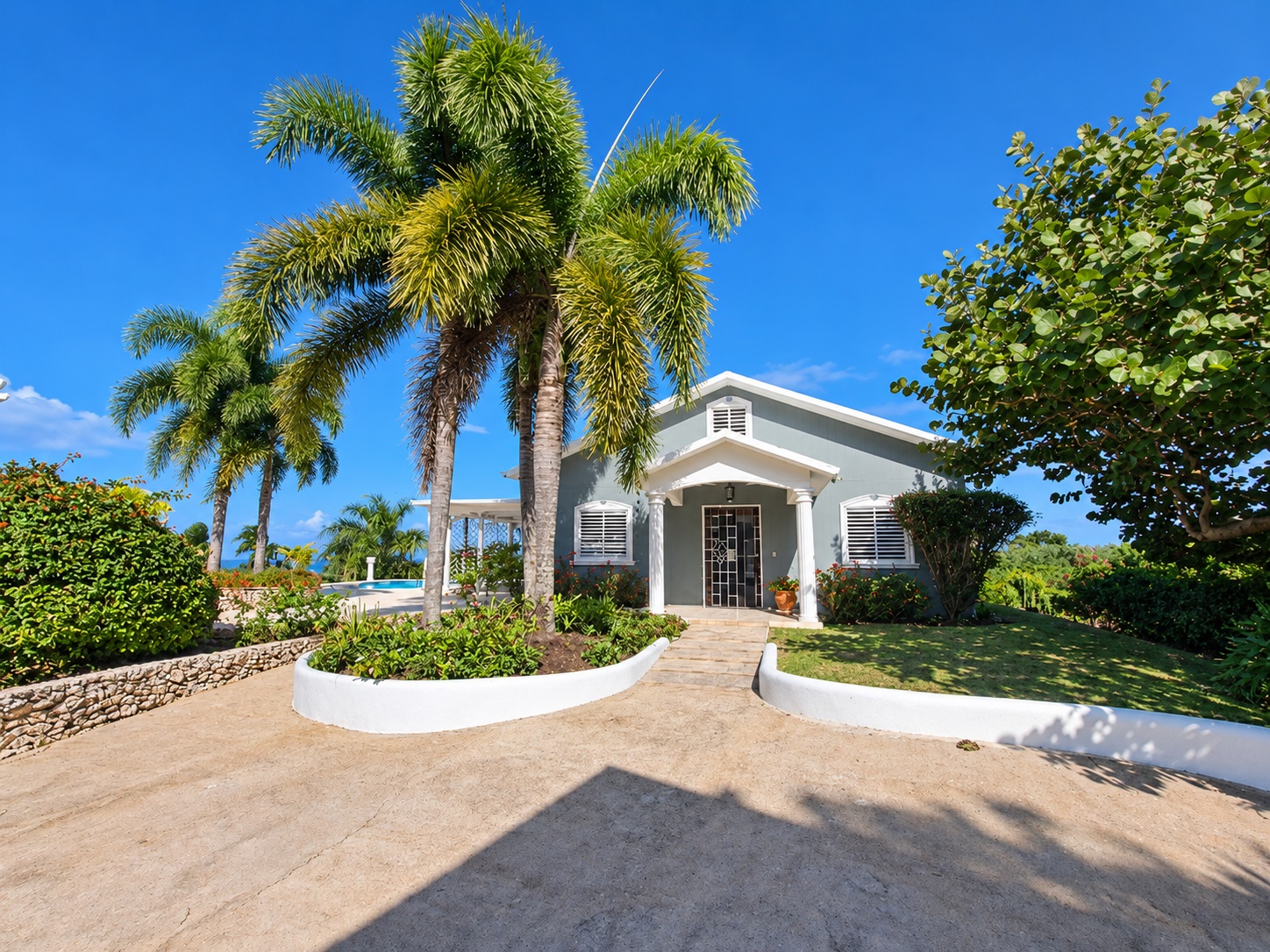 Tropical home with palm trees and swimming pool under a clear blue sky.