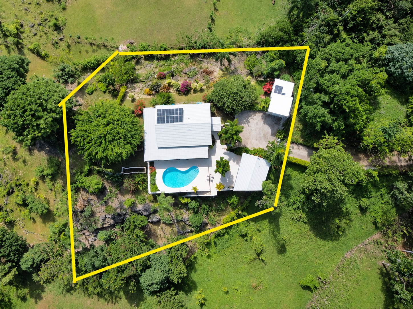 Aerial view of a modern house with a swimming pool and solar panels, surrounded by lush greenery.