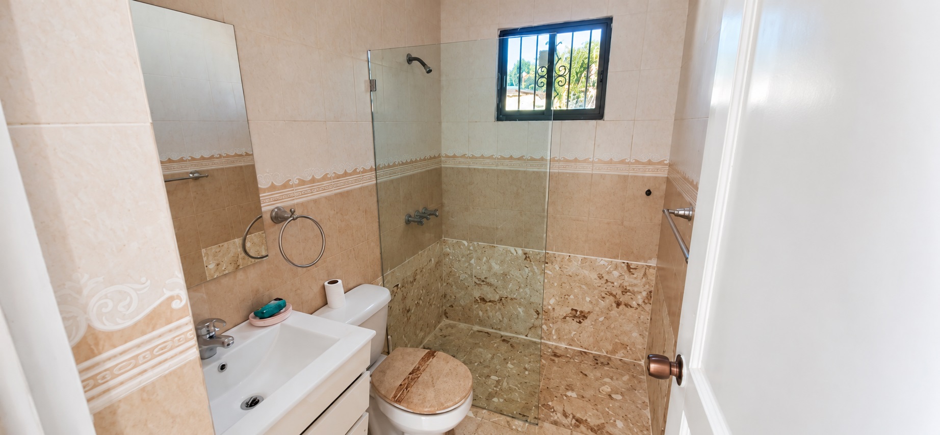 Small beige tiled bathroom with white sink, toilet, and glass shower.