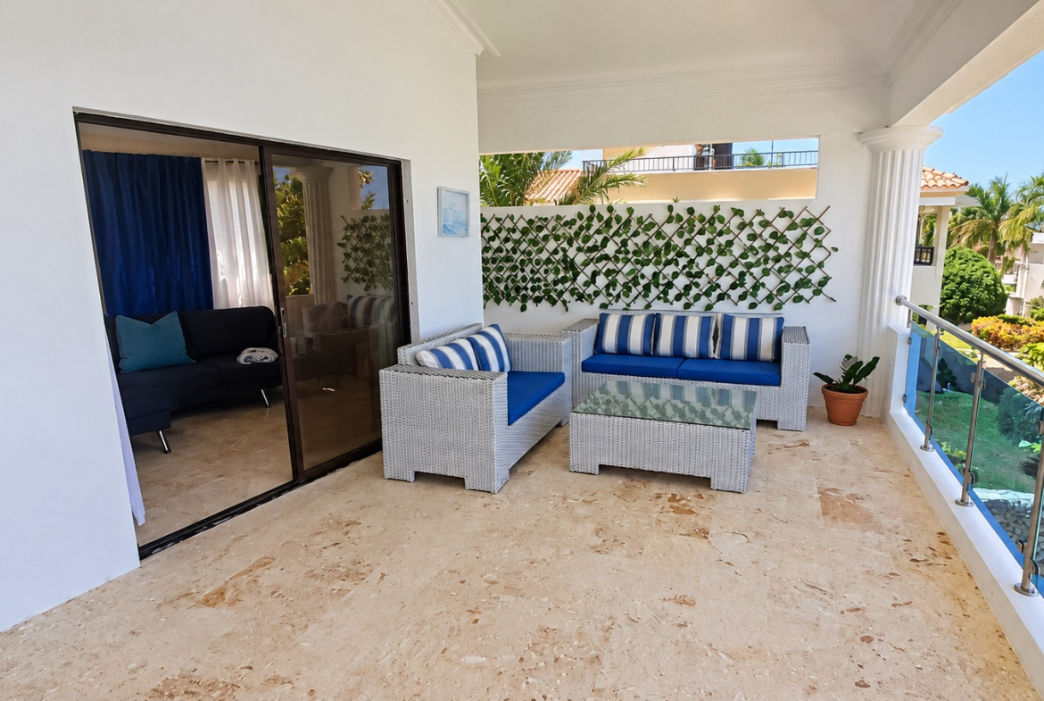 Outdoor patio furniture with blue and white striped cushions overlooks a tropical garden.