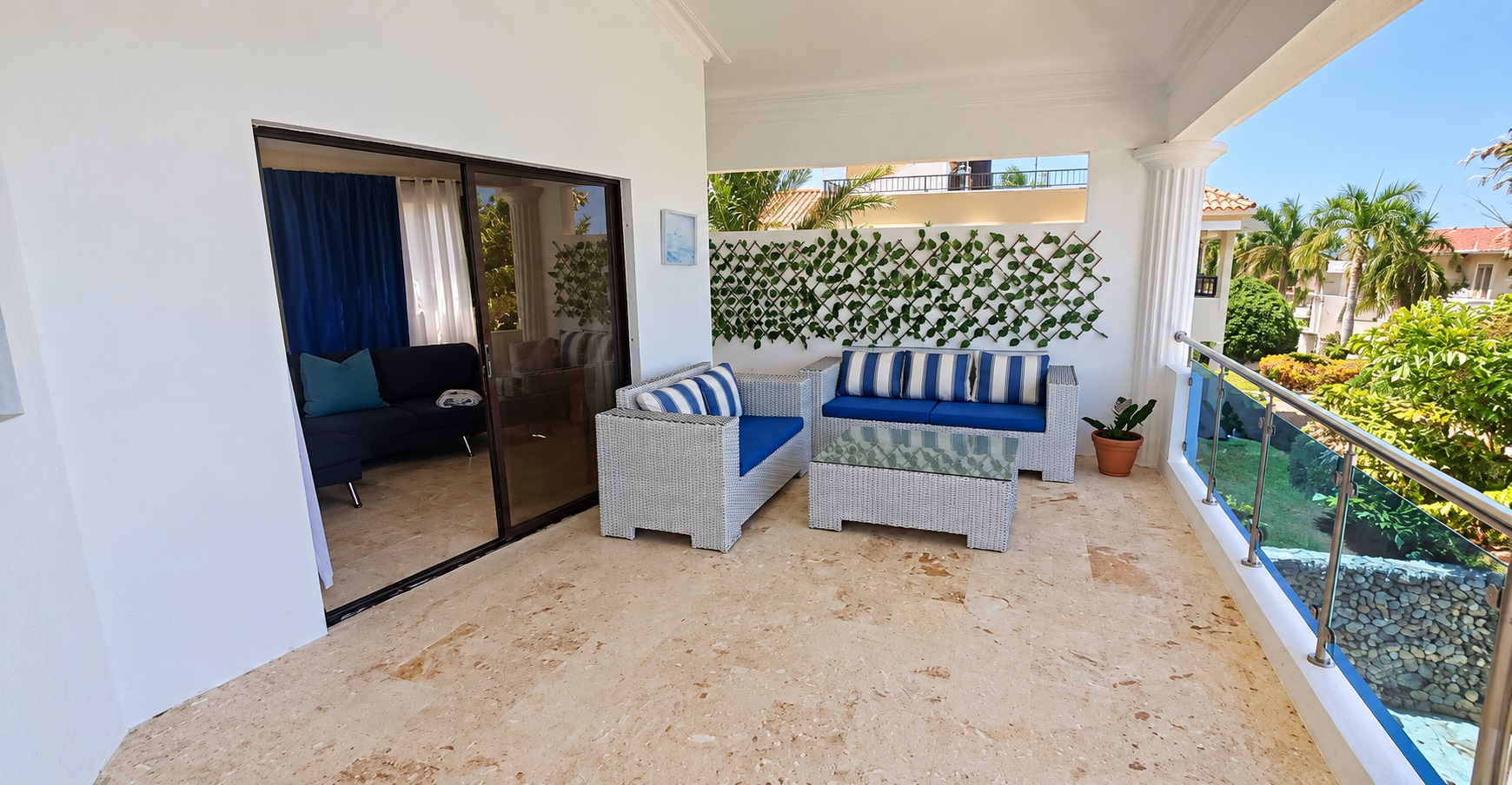 Outdoor patio furniture with blue and white striped cushions overlooks a tropical garden.