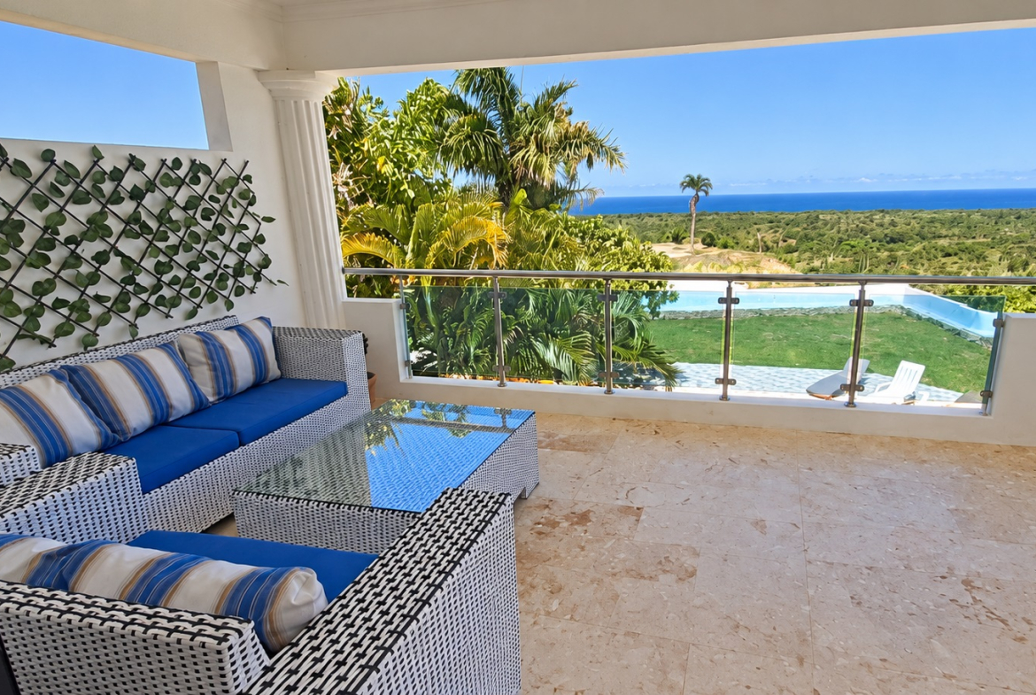 White wicker patio furniture with blue cushions on a terrace overlooking a tropical ocean view