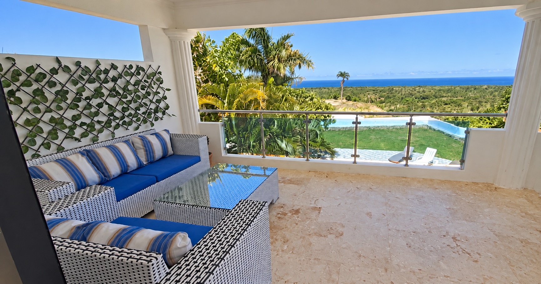 White wicker patio furniture with blue cushions on a terrace overlooking a tropical ocean view
